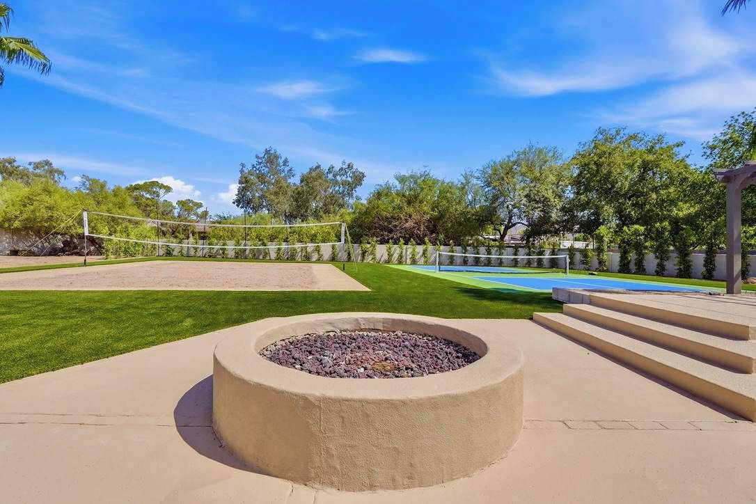 A backyard with a fire pit, a volleyball net, and a pool.
