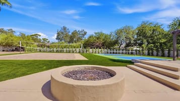 A backyard with a fire pit, a volleyball net, and a pool.