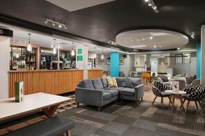 Un hall d’hôtel moderne doté d’un bar, d’un espace salon et d’un comptoir d’accueil.