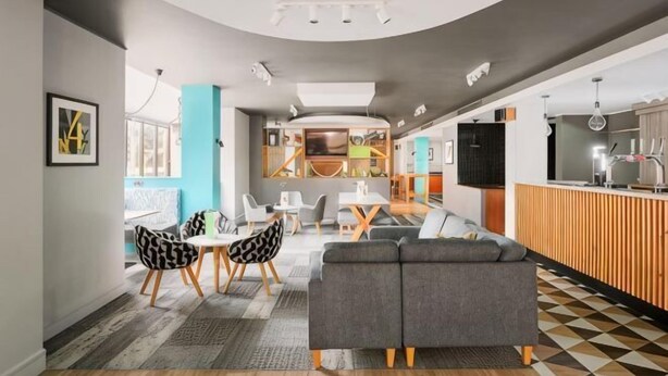 A modern interior with a sofa, dining table, chairs, and a kitchen area. - Holiday Inn NORTHAMPTON by IHG (Northampton)