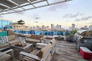 Terraza en la azotea con mobiliario exterior, una parrilla y vistas al horizonte de la ciudad.