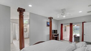 Un dormitorio con una cama grande, columnas de madera, un ventilador de techo y un televisor.