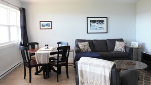 A living room with a dining table, chairs, a sofa, and two framed pictures on the wall. - Water Front Cottage- 10 Min Walk To Barachois Beach, Minutes to North Rustico (North Rustico)