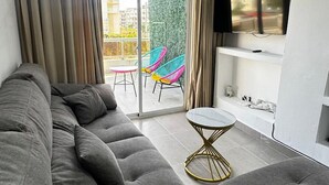 A modern living room with a grey sofa, a small round table, colorful chairs, and a TV mounted on the wall. - Refuge of LOVE in Santo Domingo East.  (Santo Domingo Este)