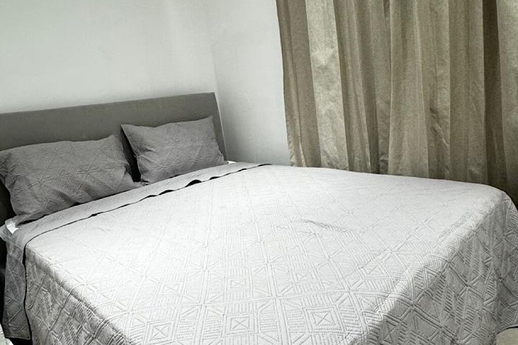 A bed with a geometric patterned bedspread, a grey headboard, and a window with curtains.