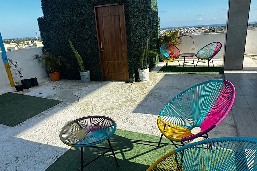 A rooftop terrace with colorful chairs, a wooden door, and potted plants.