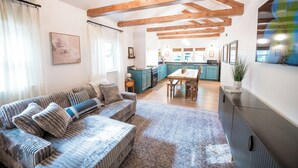 Amplia sala de estar con sofá, vigas de madera, una mesa de comedor y una cocina al fondo.