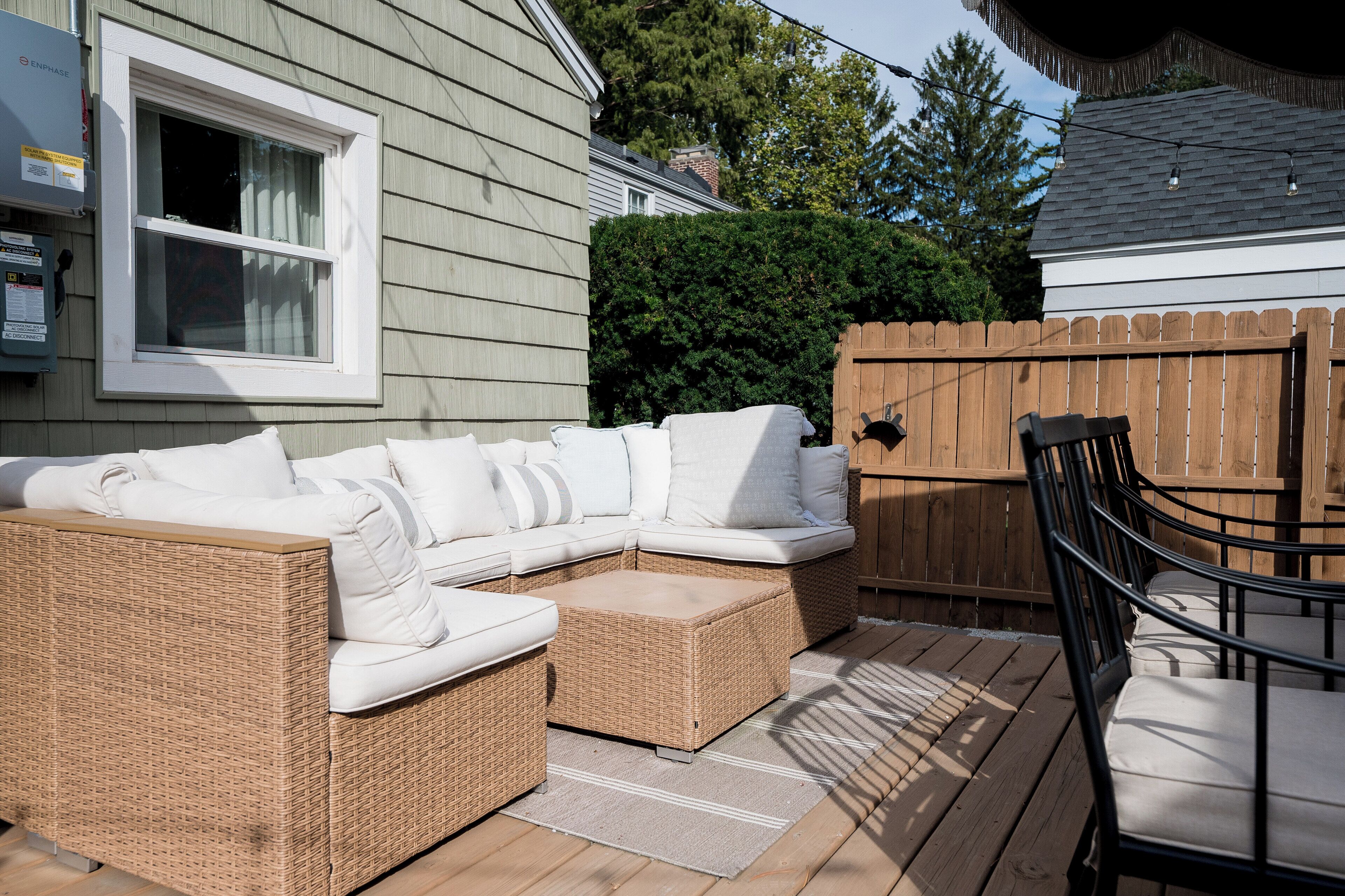 Un sofá modular de mimbre con cojines, una terraza de madera y una valla de madera.