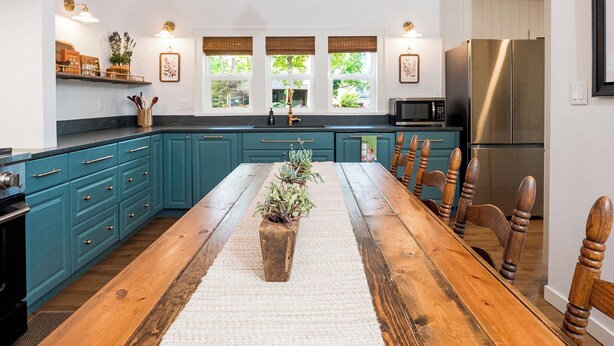 Una cocina con armarios color turquesa, una mesa de comedor de madera y una lámpara colgante.