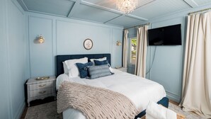 Un dormitorio con cama, mesitas de noche, televisión y una araña.