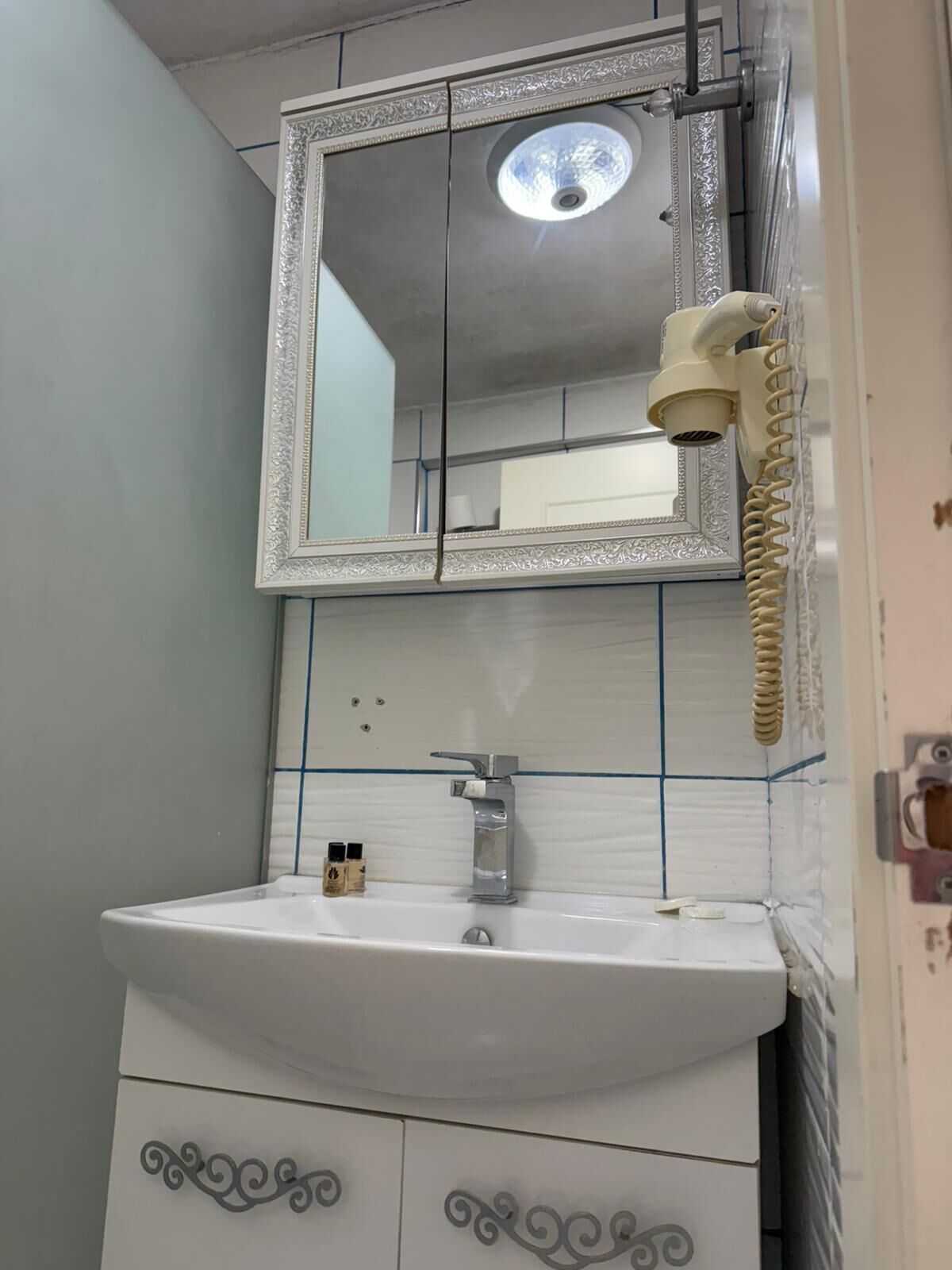 Un bagno con un lavandino bianco, uno specchio con cornice decorata e un asciugacapelli montato a parete.