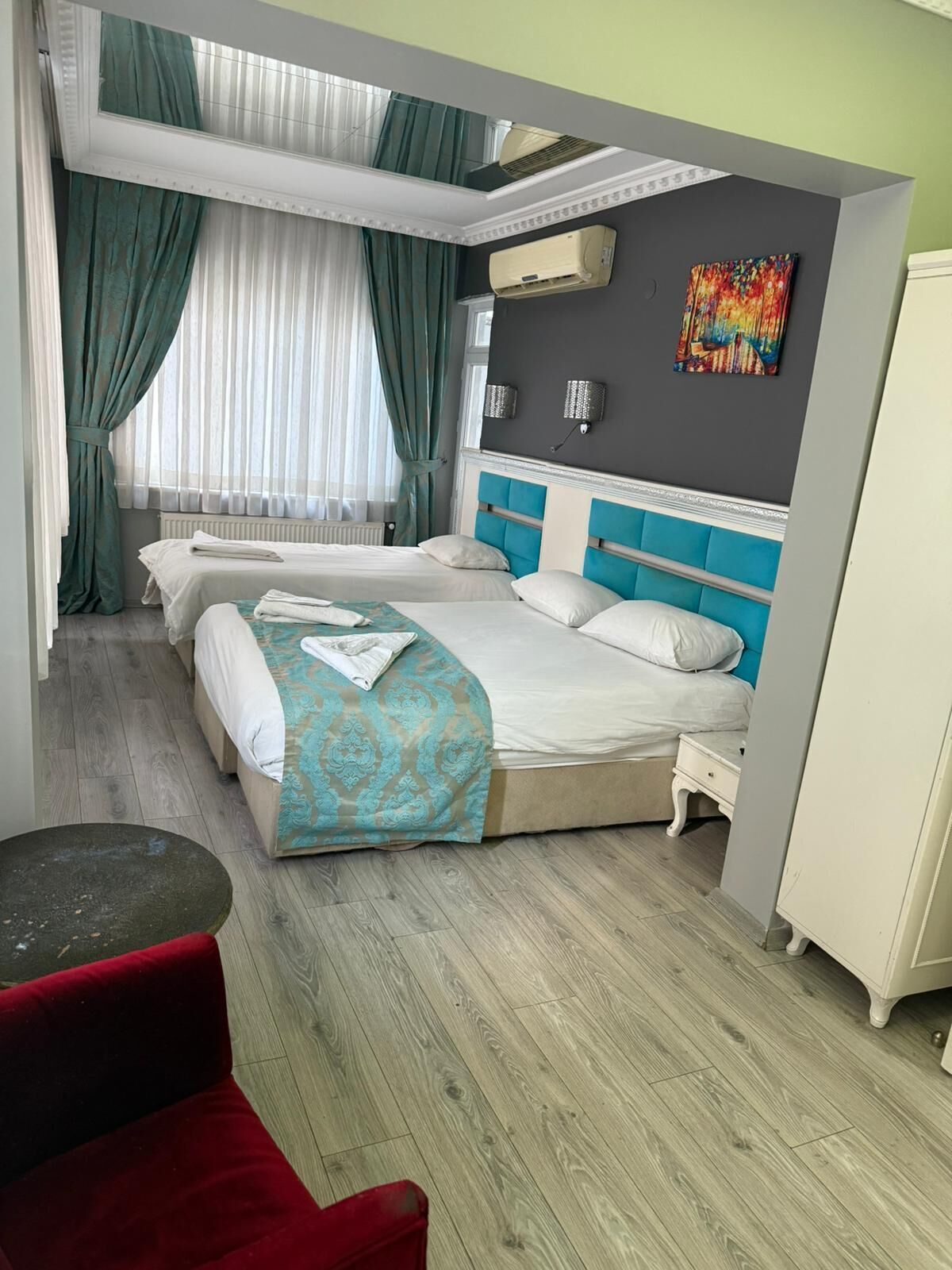 A hotel room with two beds, a red chair, a small table, and a window with curtains.