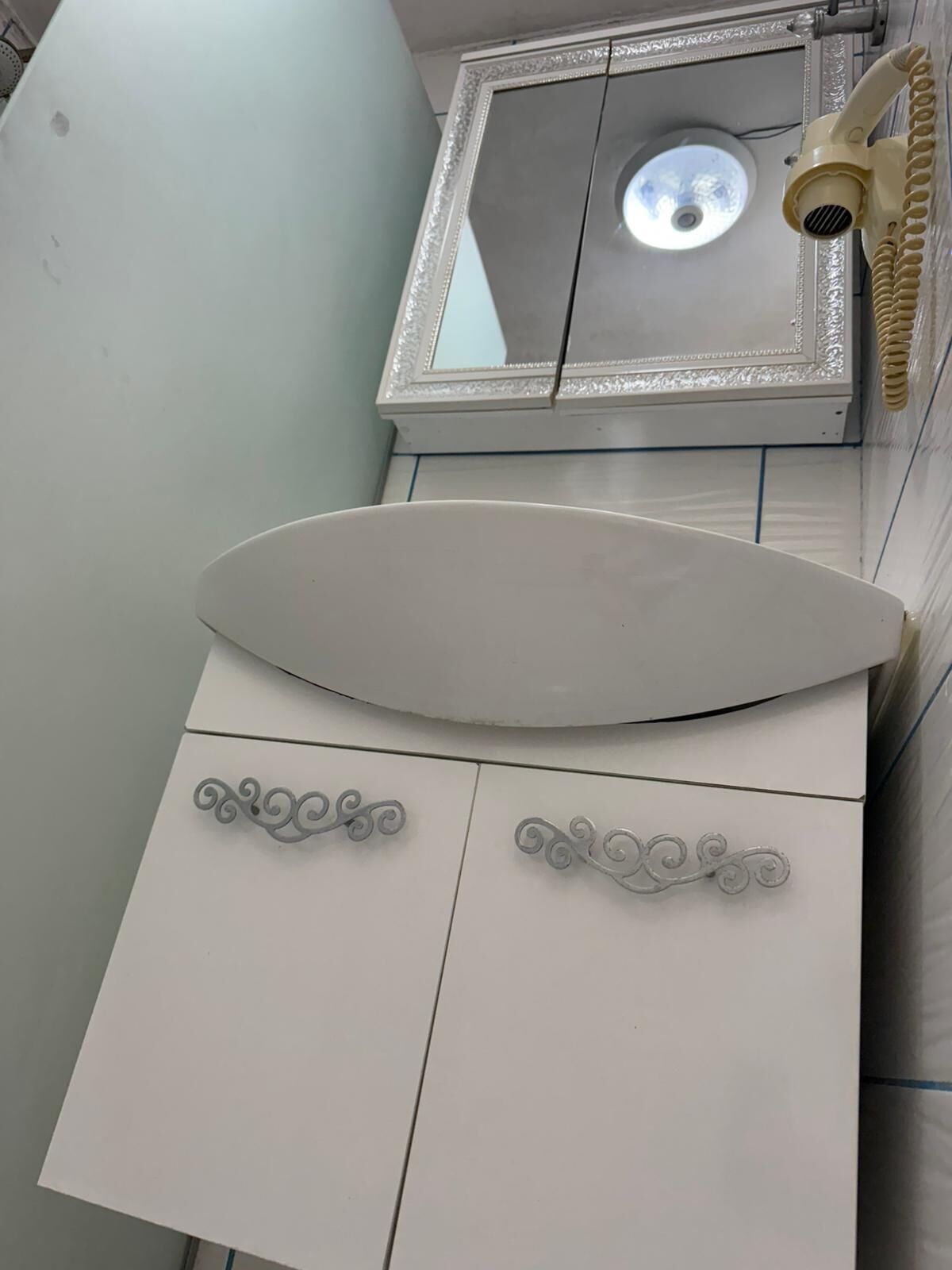 A bathroom with a white sink, a mirror with a decorative frame, and a handheld showerhead.