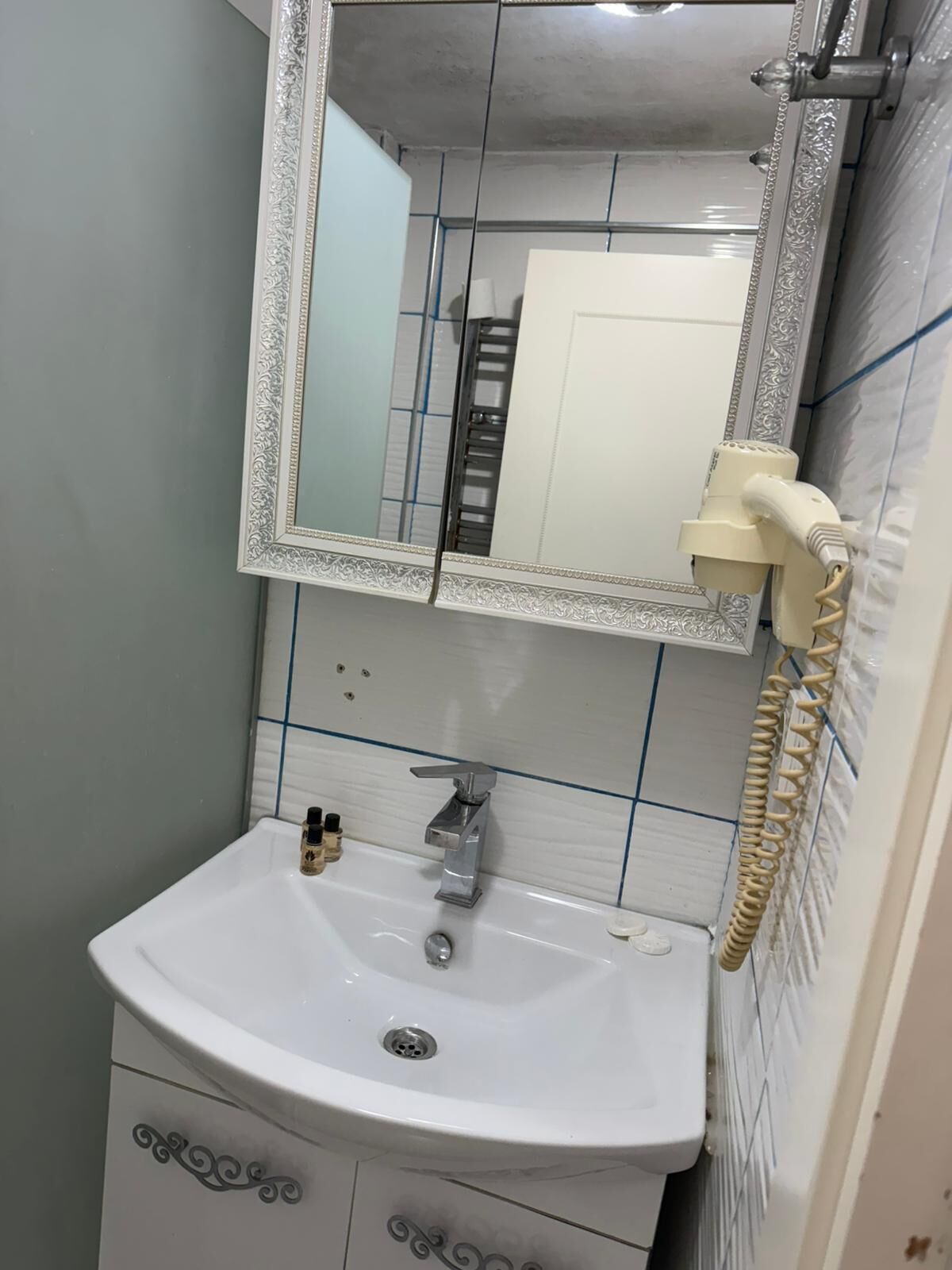 A bathroom with a white sink, a mirror with an ornate frame, and a telephone mounted on the wall.