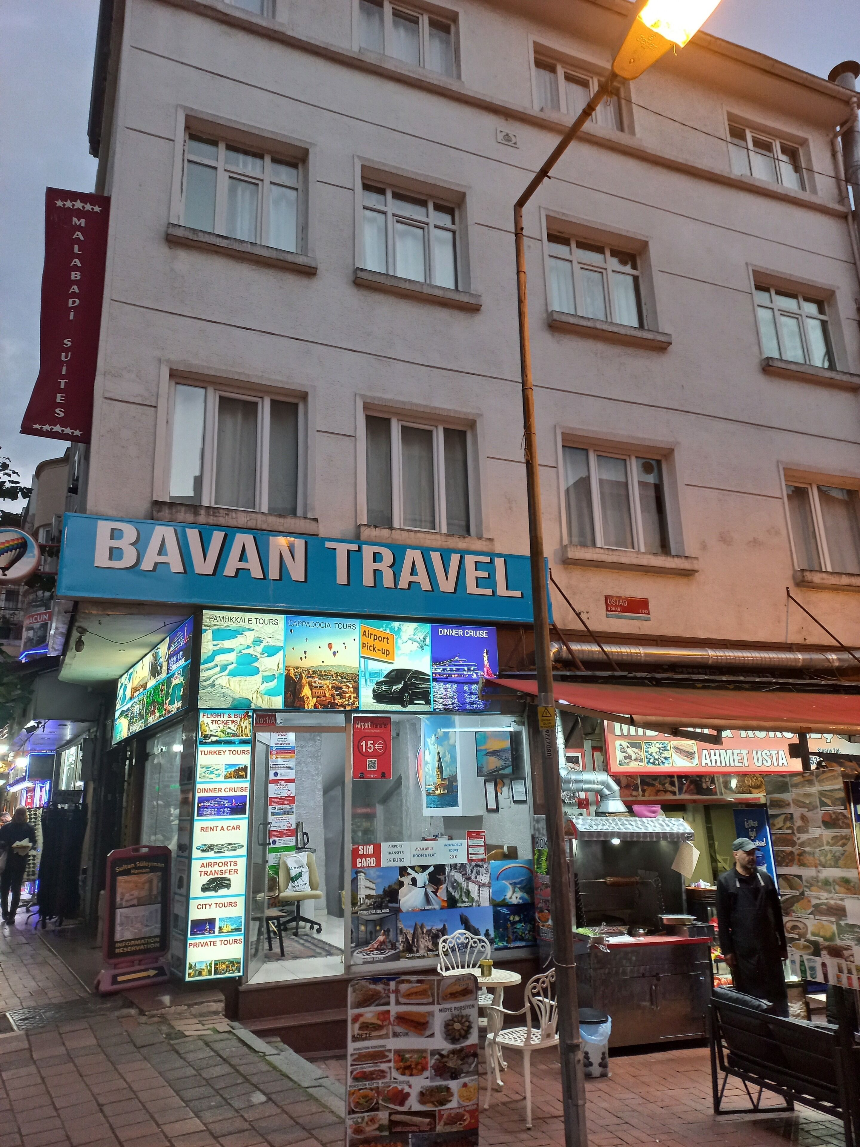 A travel agency named "BAVAN TRAVEL" with a signboard advertising various tours and services like airport pick-up, dinner cruise, and city tours.
