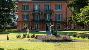 A large, multi-story building with a symmetrical facade, a central entrance, and a well-maintained garden with a bench and a sculpture. - Grand Hotel des Bains (Lavey-Morcles)