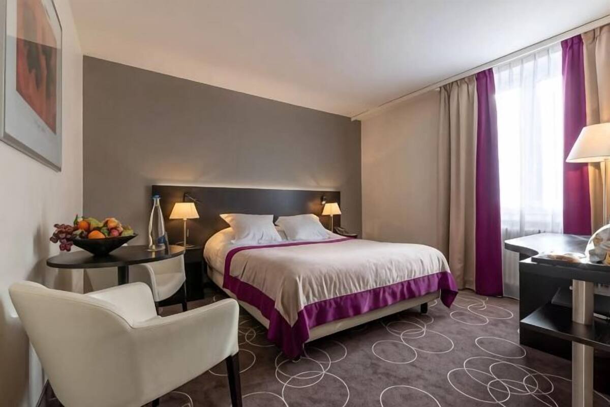 Une chambre d’hôtel comprenant un lit, des tables de chevet, un bureau, une chaise et un panier de fruits.