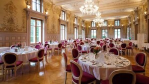 A grand banquet hall with round tables set for dining, large windows, and ornate ceiling details. - Grand Hotel des Bains (Lavey-Morcles)