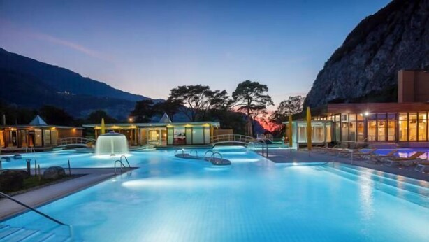 A swimming pool with a waterfall feature, surrounded by lounge chairs and a mountain backdrop. - Grand Hotel des Bains (Lavey-Morcles)