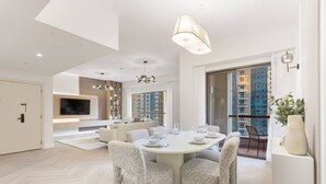 A modern living room with a round dining table, comfortable seating, a flat-screen TV, and a large window with a city view. - Cozy 3 Bedroom with walking access to JBR Beach (Jumeirah Beach Residence (JBR))