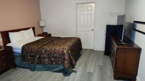 A bedroom with a bed, a dresser, a television, and a door. - Shamrock Motel (Bellingham)