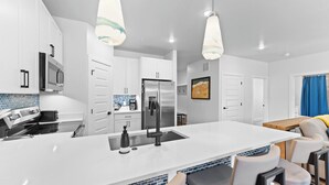Eine moderne Küche mit weißen Schränken, einem Edelstahlkühlschrank und einer zentralen Kochinsel mit Sitzgelegenheiten.