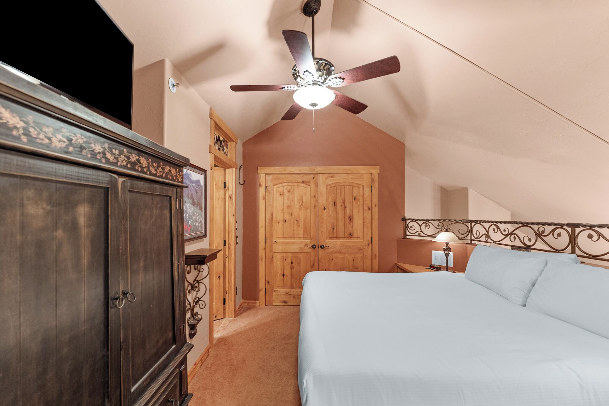 Une chambre à coucher avec un lit, un ventilateur de plafond, une armoire en bois et une porte.