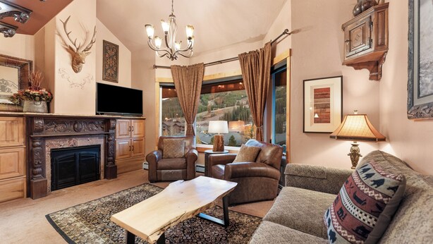 A cozy living room with a fireplace, leather sofas, a coffee table, and a large window offering a scenic view. - Tm504c1 (Copper Mountain)