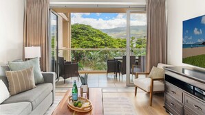 Ein modernes Wohnzimmer mit einer Couch, Sesseln, einem Esstisch mit Getränketablett, einem Fernseher und einem Balkon mit schöner Aussicht.