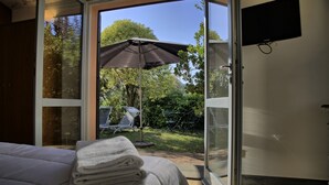 A bedroom with a bed, a stack of towels, a sliding glass door leading to a patio with a table, chairs, and an umbrella. - Villa Glicini - Delightful Cottage With Pool (Ostra)