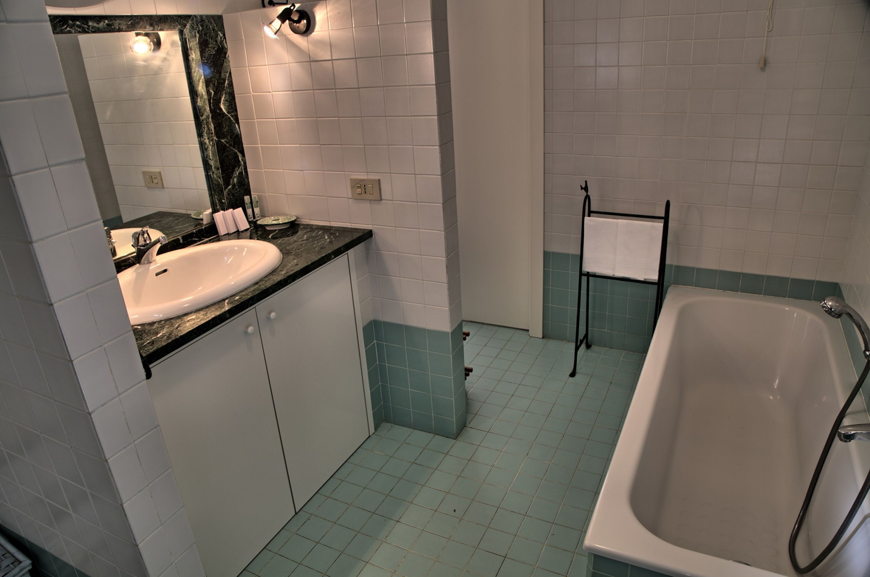 A bathroom with a white sink, a mirror with a marble backsplash, a bathtub, and light blue tiled flooring.