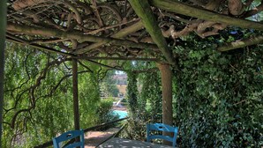 Un área de estar al aire libre con techo, que incluye una mesa y sillas, rodeada de abundante vegetación y una vista a un paisaje lejano.