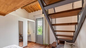 Un dormitorio con techo de madera, una escalera y vista de un jardín a través de una puerta.