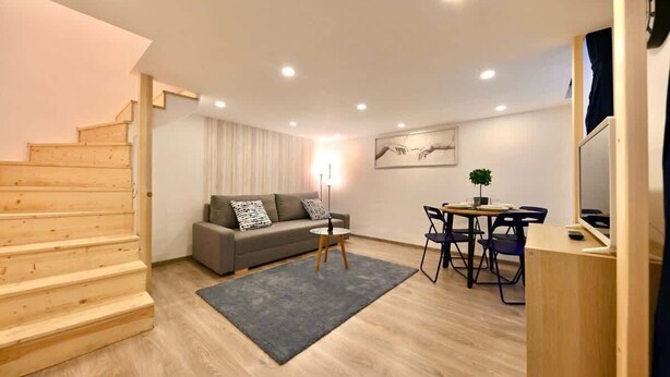Un salon moderne avec un escalier, un canapé, une table à manger et un téléviseur.