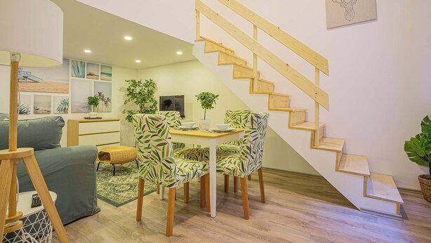A modern living room with a wooden staircase, a dining area with patterned chairs, and a green sofa. - Cosy flat in Akácfa str., Aya (Budapest)