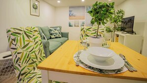 A dining area with a wooden table set for two, a green sofa, and a potted plant. - Cosy flat in Akácfa str., Aya (Budapest)
