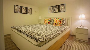 A bedroom with a bed, a nightstand, a lamp, and wall art. - Cosy flat in Akácfa str., Aya (Budapest)