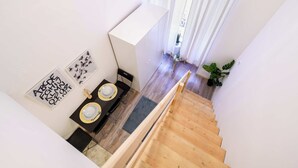 Eine Treppe führt zu einem Essbereich mit einem Tisch für zwei Personen, einem weißen Schrank und einer Pflanze.