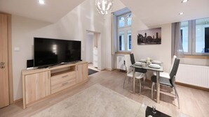 Una sala de estar moderna con televisor de pantalla plana, muebles de madera, una mesa de comedor con sillas y una pintura de un paisaje urbano.