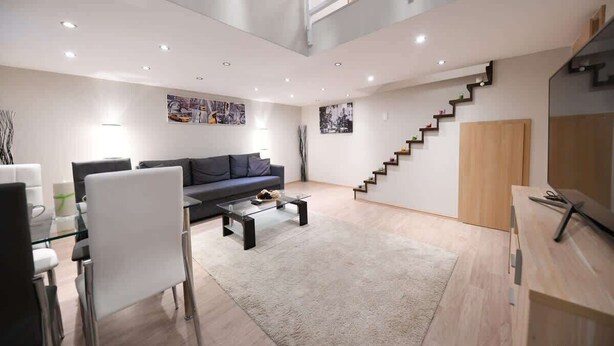 Una sala de estar moderna con un sofá, una mesa de centro, sillas, una escalera y un televisor sobre un mueble de madera.