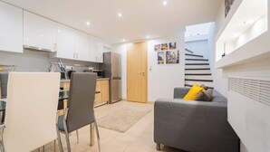 Un espacio habitable compacto con kitchenette, comedor y sofá con vista a las escaleras.