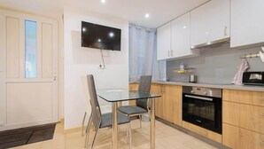 Una cocina moderna con una mesa de comedor de vidrio, un televisor de pantalla plana, armarios de madera y un horno empotrado.