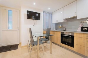 Uma cozinha moderna com mesa de jantar de vidro, televisão de tela plana, armários de madeira e forno embutido.