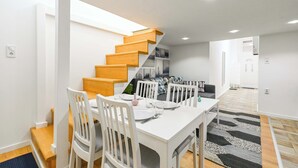 A modern dining area with a white table and chairs, a staircase with wooden steps, and a black and white rug on the floor.