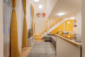 Un intérieur moderne avec un escalier, un canapé, un téléviseur et des œuvres d’art accrochées aux murs.