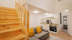 A modern apartment with a wooden staircase, a grey sofa with yellow cushions, a kitchen with white cabinets, and a black refrigerator. - Klauzal  · 2 bedroom downtown flat in Budapest, Lisa (Budapest)