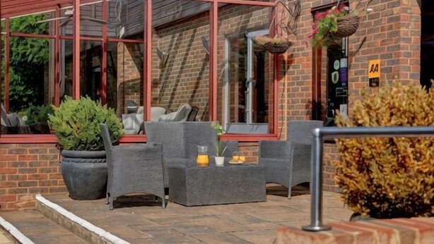An outdoor seating area with wicker furniture, potted plants, and a brick building with a red frame. - The Watermill Hotel, Sure Hotel Collection by Best Western (Bourne End)
