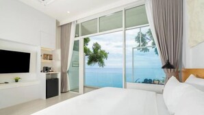 A modern hotel room with a large bed, a flat-screen TV, a small kitchenette, and a balcony with a view of the sea. - Anona Sunset Boutique (Phuket)