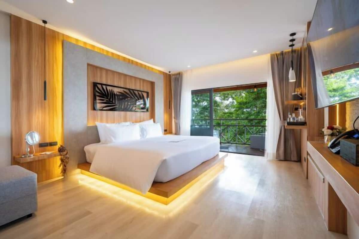 A modern bedroom with a large bed, a bedside table, a mirror, and a view of greenery outside.
