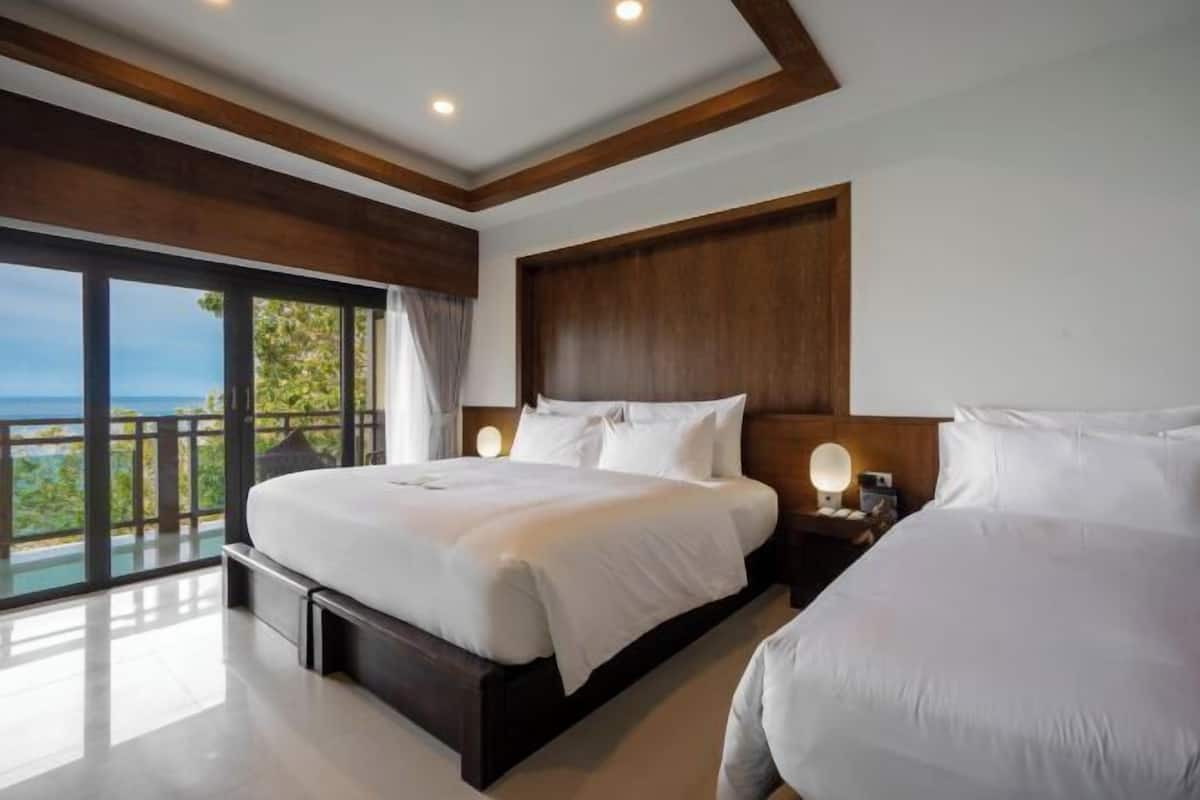 A bedroom with a large bed, a bedside table with a lamp, and a view of the sea.